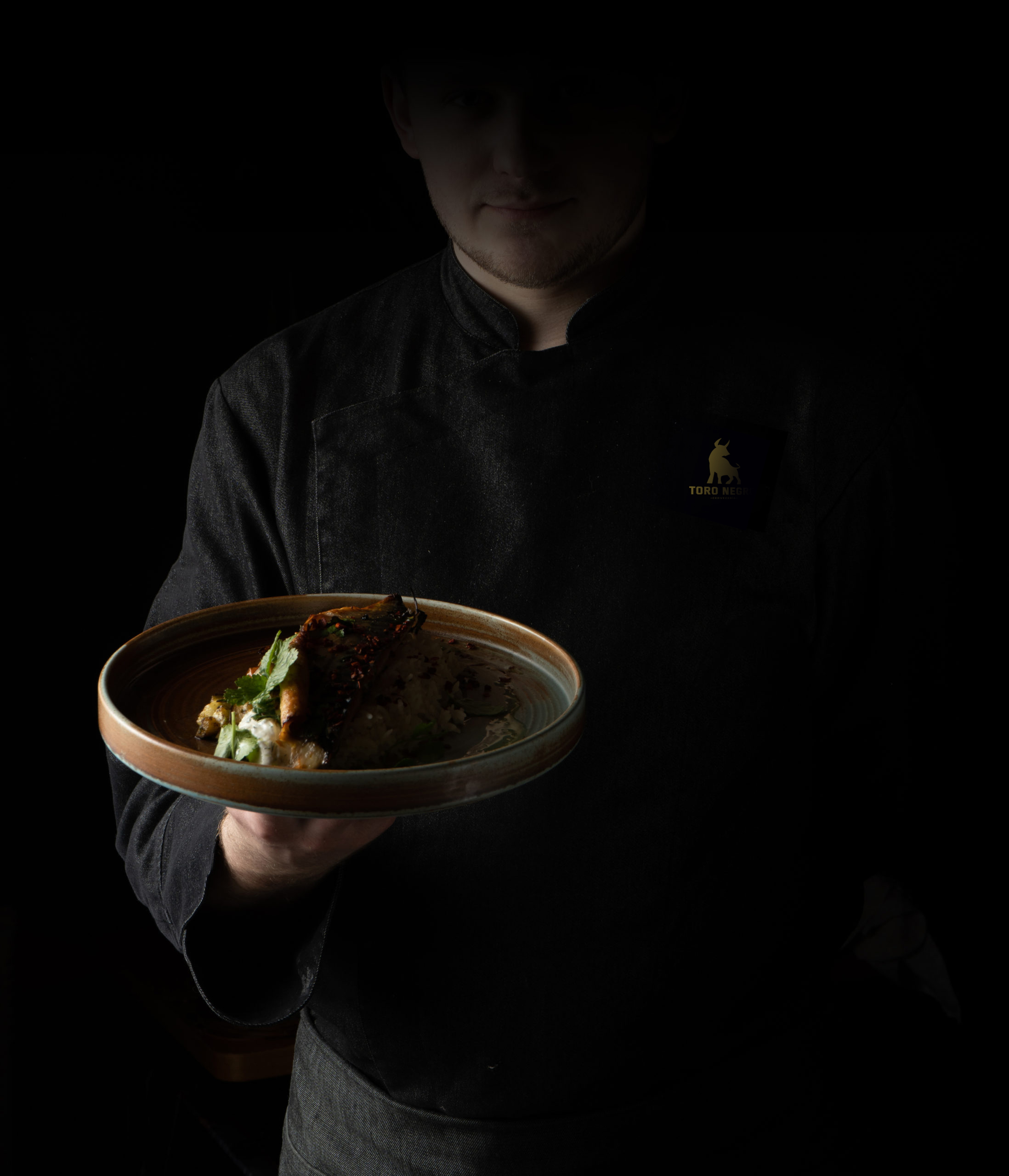 cook-black-chef-s-jacket-serves-cooked-dish-plate-scaled